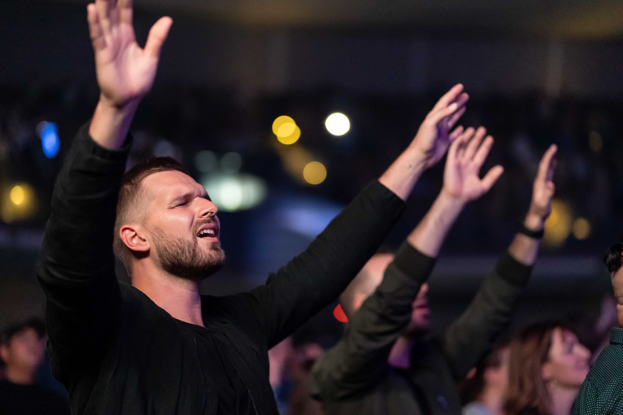 Hombre con las manos en alto y los ojos cerrados entre una multitud